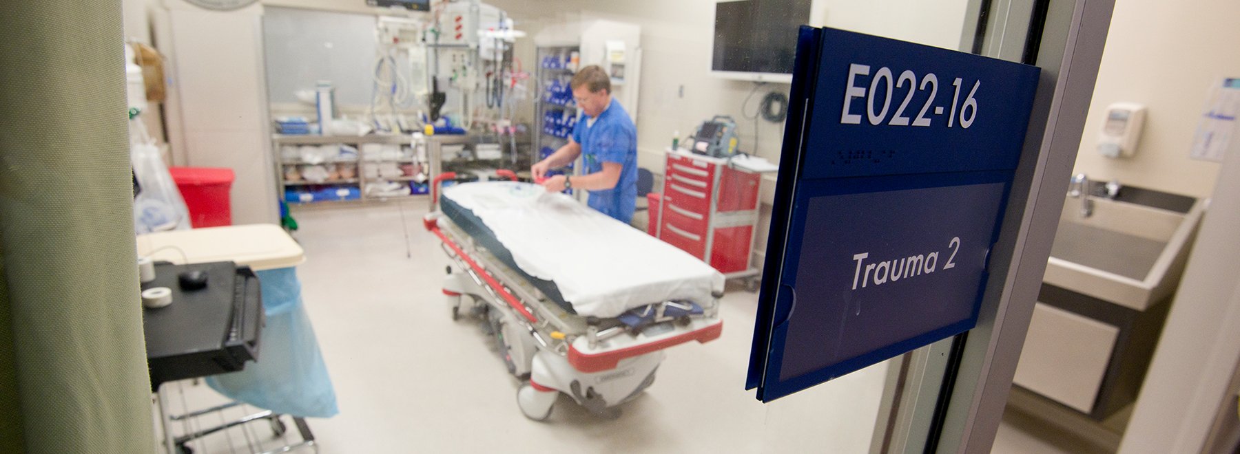Male staff member readying a hospital bed in an empty trauma room